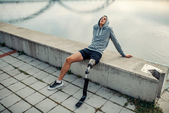 A relaxed sportsman with artificial leg sitting alone on the quay and relaxing.