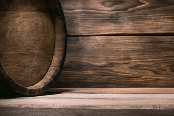 Wooden barrel of wine stands on wooden table against background of wooden wall illuminated by soft light in rustic style in brown tones of horizontal position.