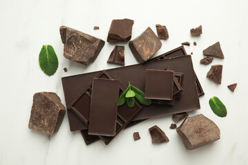 Tasty dark chocolate pieces with mint on white table, flat lay