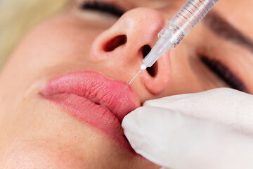 Young lady getting botox injection for bigger, fuller lips. The woman in the beauty salon. Plastic surgery clinic.