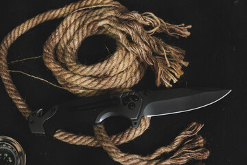 Tactical folding knife for survival, active lifestyle and recreation, on rope background and dark background.
