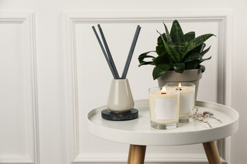 Burning soy candles, freshener and houseplant on white wooden table indoors. Space for text