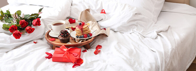 Tray with tasty breakfast, rose flowers and gift on bed. Valentine's Day celebration