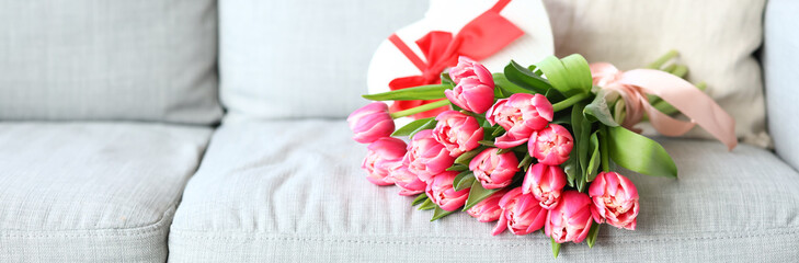 Beautiful bouquet of tulip flowers with gift on sofa