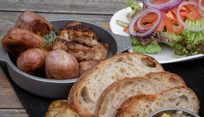 Traditional asado criollo plate. Closeup view of chorizos, pork sausages, grilled sweetbreads, potatoes, bread, and a traditional salad with lettuce, tomato and onion.
