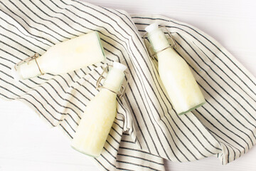 Pouring homemade kefir, buttermilk or yogurt with probiotics. Yogurt flowing from glass bottle on white wooden background. Probiotic cold fermented dairy drink. Trendy food and drink. Copy space left