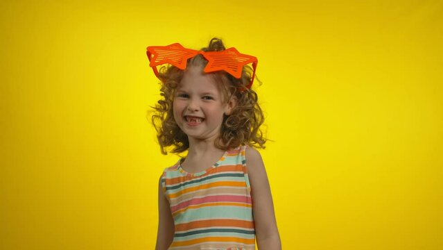 Little curly girl in funny star glasses with charming toothless smile is dancing