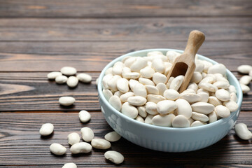 Raw white beans, bowl and scoop on wooden table, closeup. Space for text