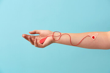 Female hand with medical plaster and red paper blood drop on color background. Donation concept