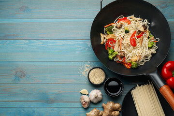 Stir fried noodles with mushrooms, chicken and vegetables in wok on light blue wooden table, flat lay. Space for text