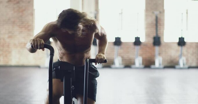 He gives it his all. Fit and active young man doing a workout using an exercise bike at a gym. Muscular guy at a health club working out with an exercise machine. Health, wellness and sport concept