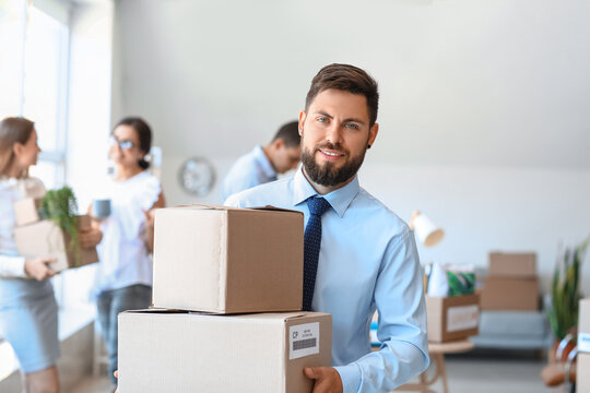 Handsome man holding boxes with things in office on moving day
