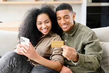 Online transaction, payment. Multiracial man holding credit card and using smartphone for shopping with his lovely woman. Dark skinned couple making purchases online