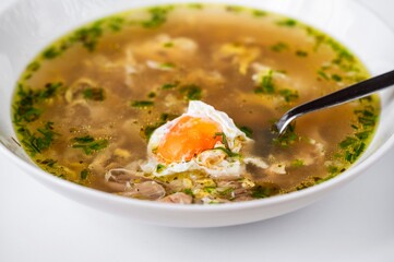 Poultry soup with meat, garlic and poached egg in white plate.