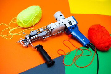 A tufting gun with multicolored yarns against a bright colored background. - 484505846