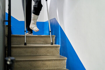 Unrecognizable man with crutches and broken leg walks down the stairs at home