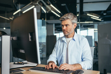 Experienced worker gray-haired businessman works at the computer in a modern office