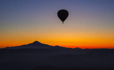 Hot air balloon flying taking off at sunrise over landscape at Cappadocia Turkey