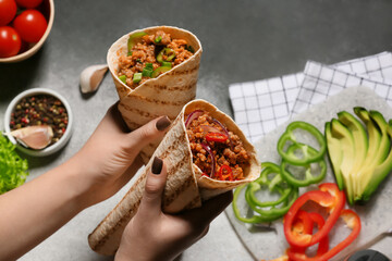 Woman holding tasty burritos on grey background