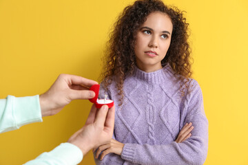 Young man proposing to his displeased girlfriend on color background