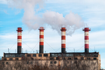 Fototapeta na wymiar Four factory chimneys emit puffs of smoke against the blue sky. The concept of air pollution, environment, industry and ecology, global warming.