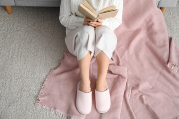 Young woman in soft comfortable slippers reading book at home