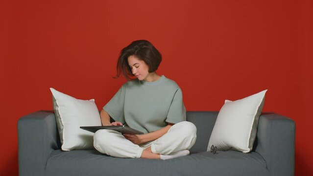 Freelancer's working day. A girl on the couch uses a laptop to work remotely during a pandemic. Red background.
