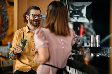 Happy man enjoys in conversation with his girlfriend while drinking cocktail in bar.