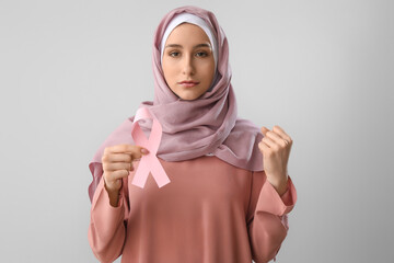 Muslim woman with pink ribbon on light background. Breast cancer awareness concept