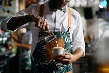 Close-up of barista makes cappuccino and adding milk while working in bar.