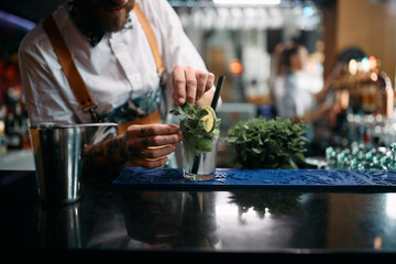 Close-up of bartender prepares mojito cocktail at bar counter.
