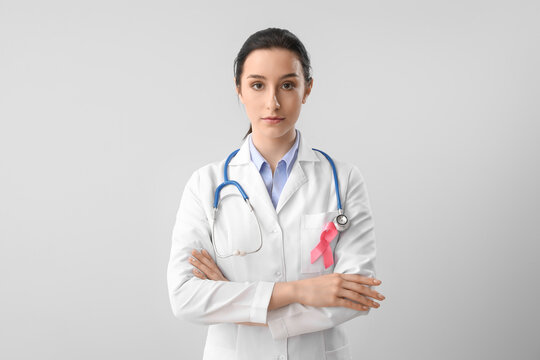 Female oncologist with pink ribbon on light background. Breast cancer awareness concept