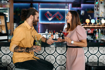 Cheerful couple have fun while drinking cocktails and talking at bar counter.