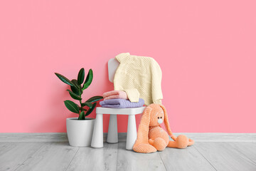 Toy, houseplant and chair with knitted sweaters for children near pink wall