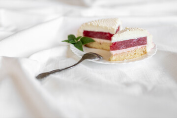 A white-pink piece of cake lies on a white plate on a light background. Delicious pastries