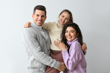 Fototapeta premium Happy little girl and her parents in warm sweaters on light background