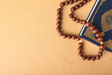 Koran and Muslim prayer beads on color background