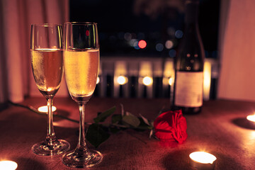 Two glasses of champagne and red rose on table, romantic date night setting 