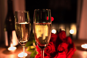 Closeup of champagne glasses on table with red roses and candle light in background, Valentine's Day