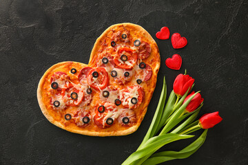 Tasty heart-shaped pizza and tulip flowers on black background. Valentine's Day celebration