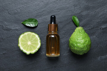 Glass bottle of bergamot essential oil and fresh fruits on black slate table, flat lay - obrazy, fototapety, plakaty