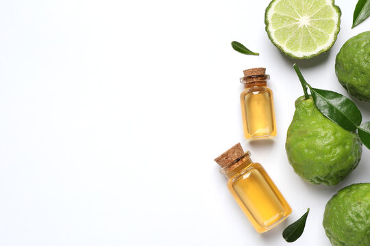 Glass bottles of bergamot essential oil and fresh fruits on white background, flat lay. Space for text