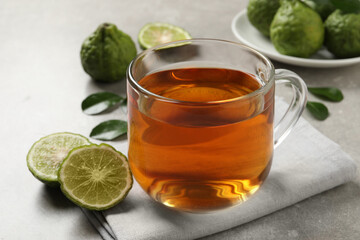 Glass cup of tasty bergamot tea and fresh fruits on light grey table, closeup