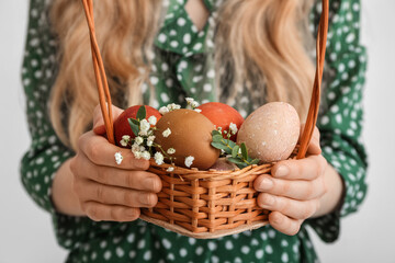 Woman holding wicker basket with painted Easter eggs on light background