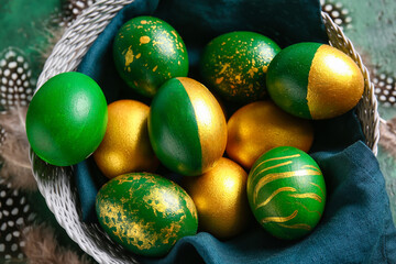 Basket with stylish Easter eggs and feathers on green background