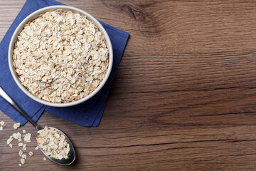 Bowl and spoon with oatmeal on wooden table, flat lay. Space for text