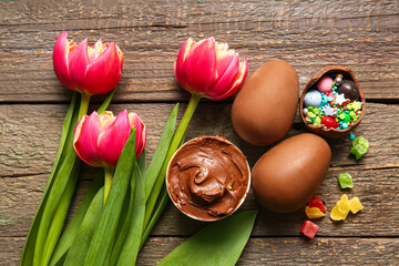 Composition with chocolate Easter eggs, different candies and flowers on wooden background