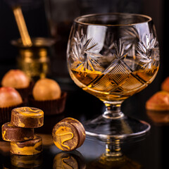 glass of whiskey with chocolate pralines on dark background
