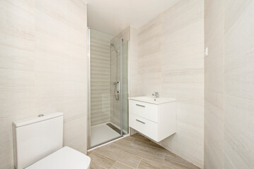 Fototapeta na wymiar Simple bathroom with white wooden furniture, glass-enclosed shower stall and white toilet bowls