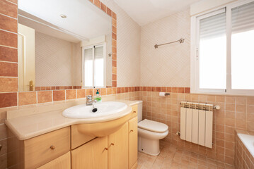 Fototapeta na wymiar Bathroom with light colored wooden cabinets and reddish and cream colored tiles